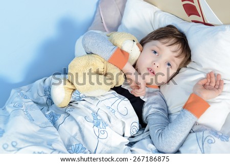 Portrait of a sick boy hugging a teddy bear lying in a bed