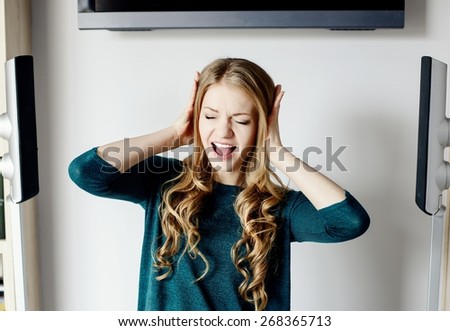 Woman covers her ears while  standing between two noisy speakers