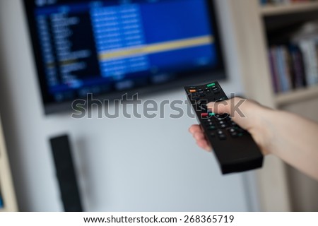 Hand holding tv remote control directs him toward the TV and changes the settings