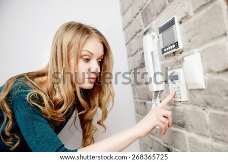 Beautiful young blond woman activates an alarm in the house. Introduces a code using the keypad