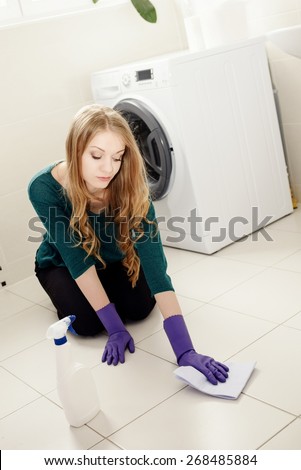 Tired beautiful blond woman washes the floor in the bathroom on her knees