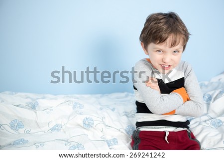 Cute 6 year old boy sitting on the edge of the bed happy with crossed arms