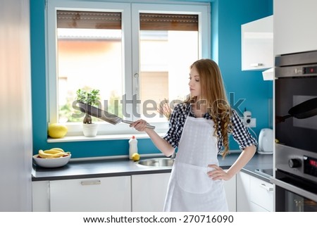Happy housewife or chef in white kitchen apron with frying pan