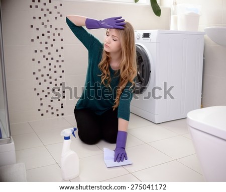 Tired beautiful young blond woman washes the floor in the bathroom on her knees