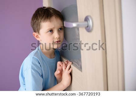 Sad, frightened child listening to a parent talking through the door with a glass pressed to his ear.