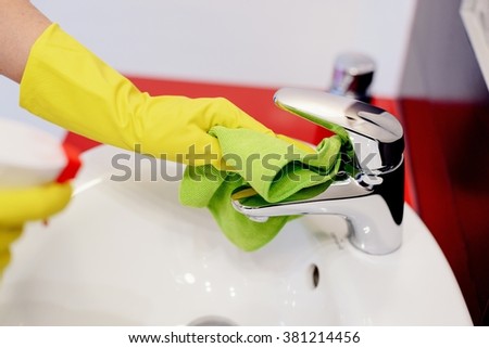 Female hands with rubber protective gloves cleaning tap with green cloth. Spring cleaning