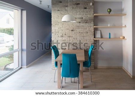 Modern dining room with wooden table, turquoise leather chairs, old grey brick wall and shelves