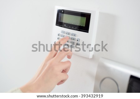 Close up on brunette woman\'s hand entering code on keypad of home security alarm. Video intercom next to alarm keypad.