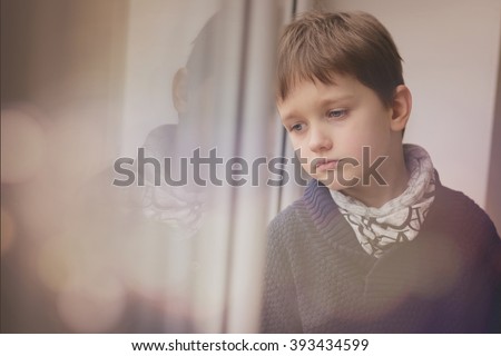 Sad thoughtful little boy looking through the window. Rainy day