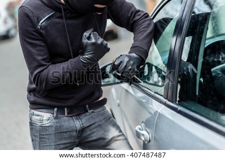 The man dressed in black with a balaclava on his head trying to break into the car. He uses a screwdriver. Car thief, car theft concept