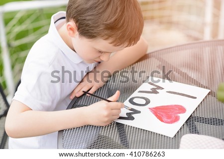 Little 7 year old boy paints greeting card for Mom on Mother\'s Day with the inscription \