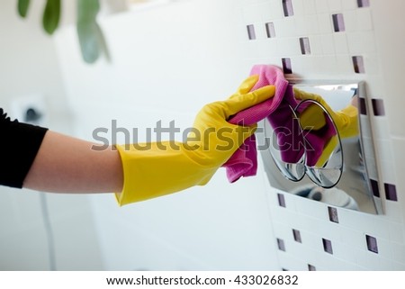 Woman in yellow rubber gloves cleaning flush button with pink cloth