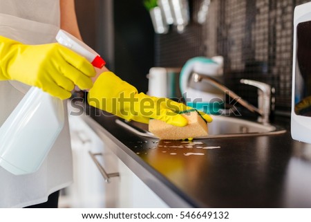 Woman cleaning kitchen cabinets with sponge and spray cleaner.