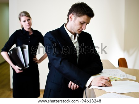 Office life scene. Young businessman signing documents and young secretary with file binders in hand.