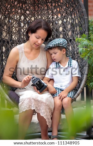 Mother and son sitting on the cane-chair and holding retro camera