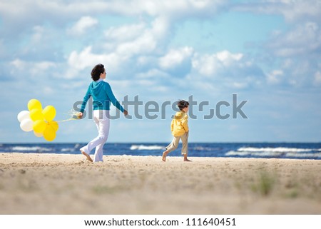 Mother and little son with yellow balloons on the beach on beautiful summer day