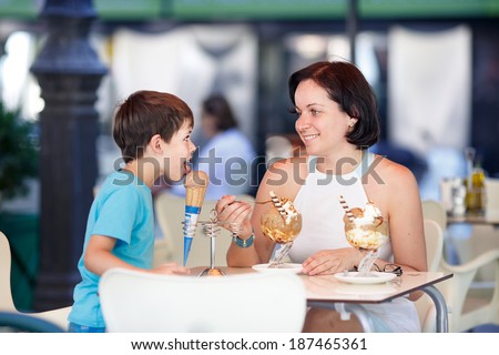 Cute little boy and his mother eating ice-cream in an outdoor cafe