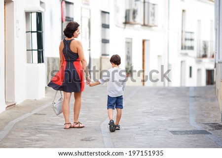 Back view of mother and her little son outdoors in city on beautiful summer day