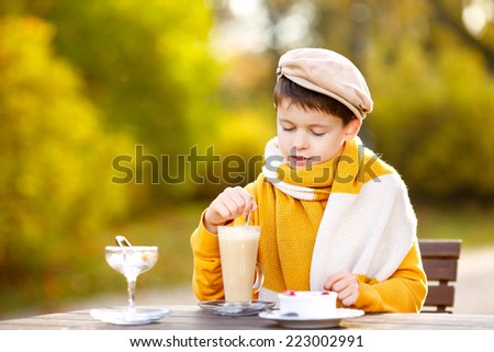 Cute little boy drinking hot chocolate in cafe on beautiful autumn day