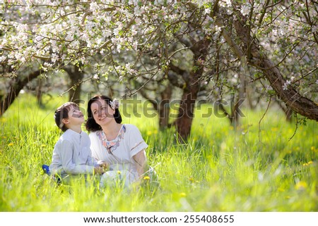 Happy young woman and her child talking and having rest in spring apple garden
