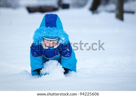 Portrait of cute 3 years old boy playing with snow outdoors