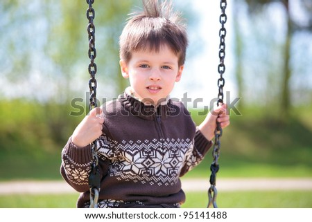 Little 3 year old boy on swing in playground outdoors