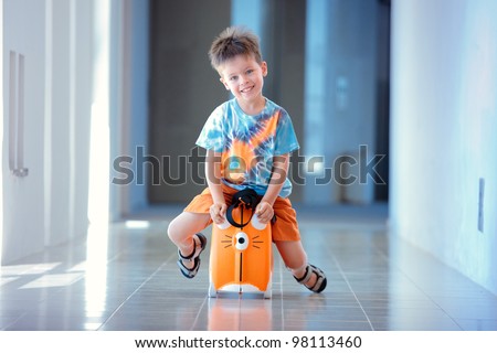 Cute three years old boy laughs and sitting on a suitcase at airport