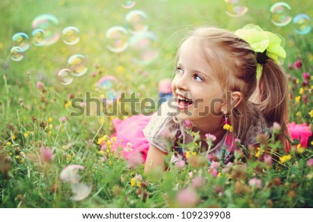 Sweet, happy, smiling six year old girl laying on a grass in a park playing with bubbles and laughing