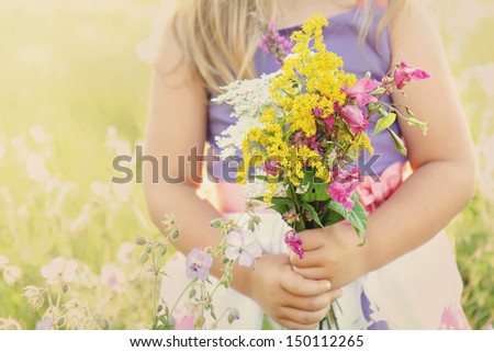 Little girl holding wild flowers bouquet on a grassy sunny summer meadow field