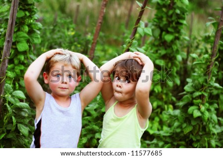 Four year old friends making funny faces among green bean plants in the garden