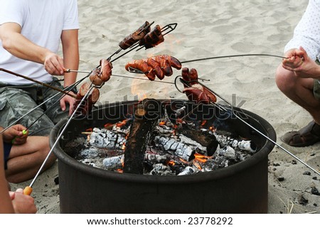 Group of friends cooking sausages on the fire on the beach