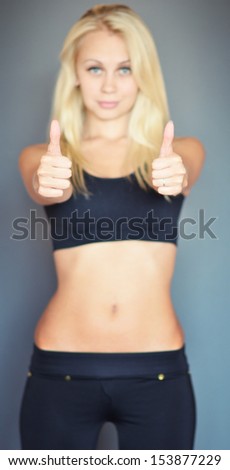 slim fitness woman showing thumbs up (focus on fingers)