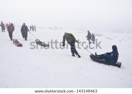 GULMARG,INDIA-APRI L 13:Sled driver carries the tourist on snow sled up to the hill before ride down on April 13,2012 in Gulmarg, Kashmir-India.Snow sled is very popular activity at Gulmarg in winter.