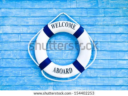 White Life buoy with welcome aboard on blue wall