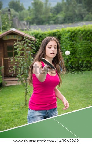 young brunette girl plays table tennis outdoors