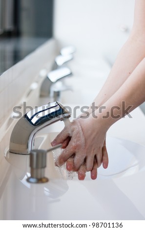 Washing hands in a public restroom (focus on the tap, hands in motion)
