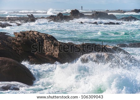 Big waves broken near stone seashore of France and lighthouse