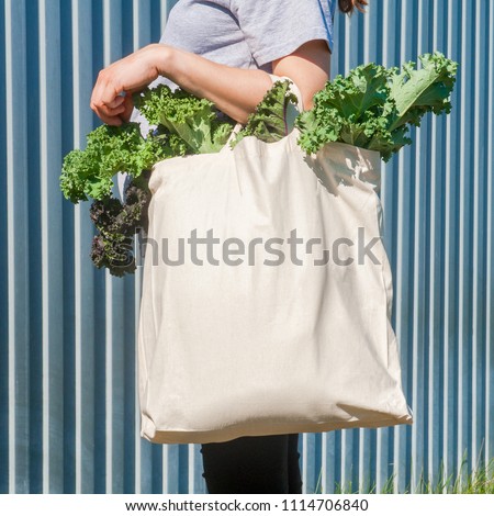 Plain flex eco-bag with green fresh kale and arm on the background of the metal fence or wall
