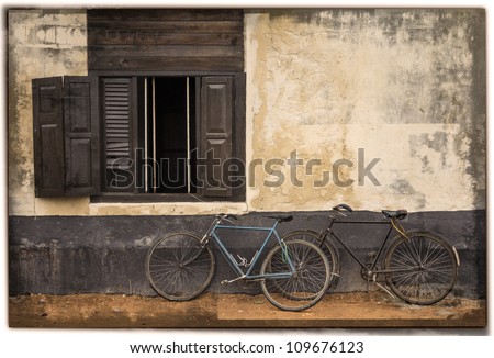 2 old bicycles lean on wall with an open window