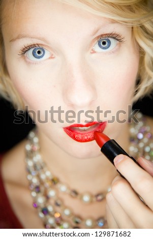Lady with amazing eyes putting lipstick (like in front of a mirror) Beautiful lady with an old fashioned style shot in studio with a black background.