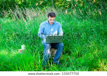 Surprised Young man outdoors with a cup and laptop in nature