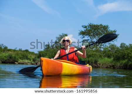 Young Woman Kayaking Alone on a Calm River and Wearing a Safety Vest