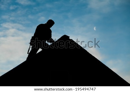 Contractor in Silhouette working on a Roof Top with blue Sky in Background