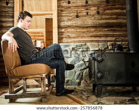 Lonely Man sitting in front of a Slow Combustion Stove and Relaxing with Slippers and Cup of Coffee.
