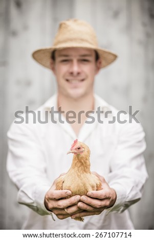 Farmer Holding a Beige Chicken in front of the Farm