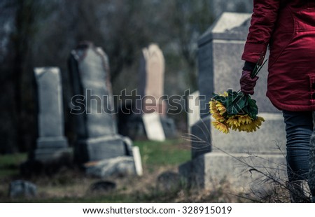 Close-up of a Sad Woman Holding Sunflowers in front of a Loved one\'s Gravestone. Focus on the Bouquet.