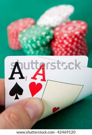 Poker hand with two aces. Some casino chips in the background over a green gaming table.