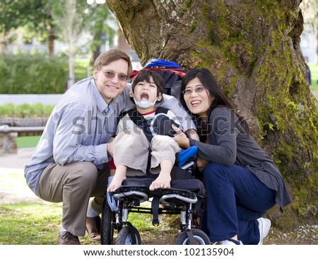 Happy disabled child in wheelchair surrounded by parents, outdoors. Cerebral palsy.