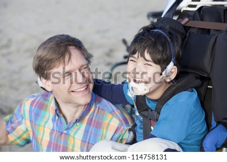 Father and disabled five year old son laughing together on beach