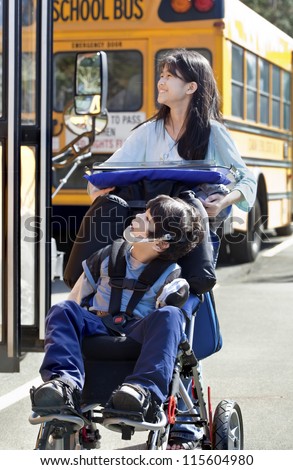 Ten year old girl  pushing disabled little boy wearing protective gear  in wheelchair  next to school bus. Child has cerebral palsy.